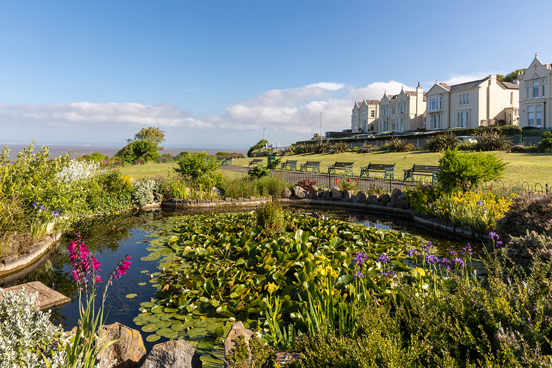 View of a public garden overlooking the sea with a pond and flowers in the foreground